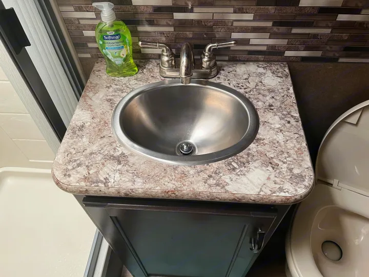 Compact RV rental bathroom with stainless steel sink, faucet, soap, and a peek of the toilet and shower area.. Thor Freedom Elite 2020
