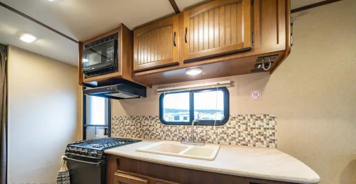 Interior view of an RV rental kitchen, featuring a dual sink, gas stove, microwave, and ample cabinet storage.. Jayco Jay Feather Ultra Lite 2015