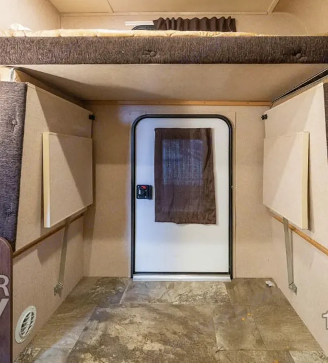 Interior view of an RV rental showing a bunk bed, main entry door, and fold-down side tables.. Jayco Jay Feather Ultra Lite 2015