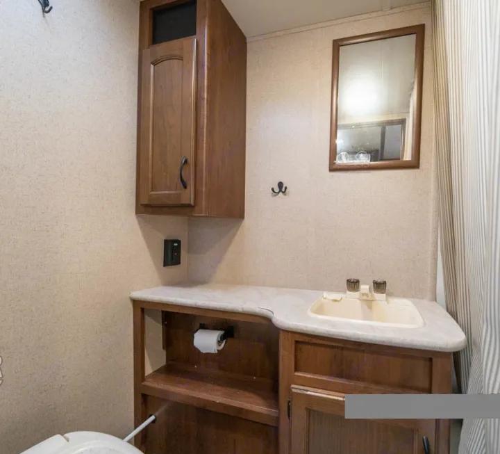 RV rental bathroom with wood vanity, sink, mirror, wall cabinet, and toilet area. Compact and functional space.. Jayco Jay Feather Ultra Lite 2015