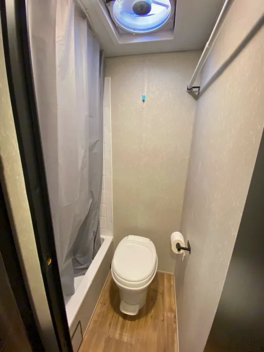 View of a compact RV rental bathroom, showing a toilet, bathtub with shower curtain, and ceiling vent.. Forest River Wolf Pup -Black Label 2021