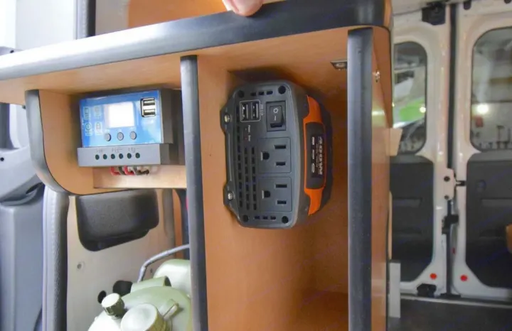RV rental van interior: a solar charge controller and power inverter mounted on a wooden shelf provide power for electronics.. Cascade Campers Ram Promaster City 2020