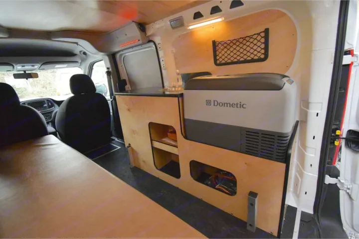 Inside an RV rental: a cozy camper van conversion with a Dometic fridge, sink, storage, and a comfy bed.. Cascade Campers Ram Promaster City 2020