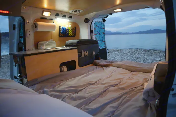 Inviting RV rental campervan interior features a comfy bed & kitchen, boasting a serene lake view. Ideal for road trips.. Cascade Campers Ram Promaster City 2020