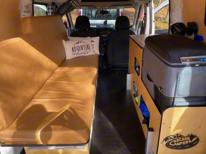 Interior of an rv rental van showing a long bench seat, a portable fridge, and storage. Ready for adventure!. Cascade Campers Ram Promaster City 2020