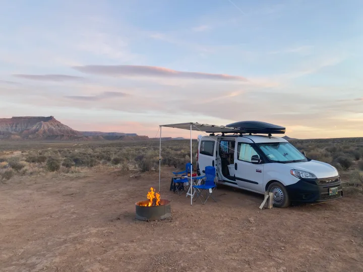 RV rental adventure in the desert: campervan with awning, chairs, and a cozy campfire. Perfect for serene camping!. Cascade Campers Ram Promaster City 2020