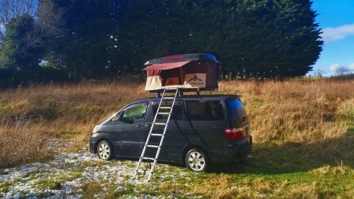 Black camper van with a deployed rooftop tent & ladder in a snowy field. Perfect for your next RV rental adventure.. Toyota Other 2022