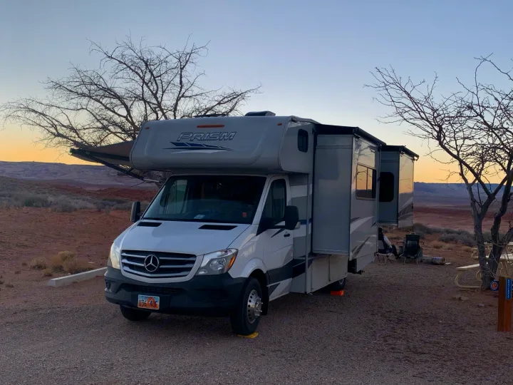 A Prism RV rental, a white and grey motorhome, set up at a scenic Utah desert campsite with awning extended.. Forest River Coachmen Prism 2020