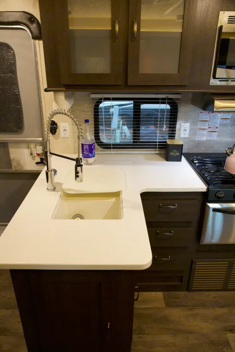 RV rental kitchen interior featuring white counters, a versatile sink with a pull-down faucet, and dark wood cabinets.. Forest River Salem 2018