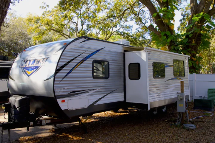 A Salem travel trailer RV rental, slide-out extended, parked at a sunny, leafy campsite.. Forest River Salem 2018