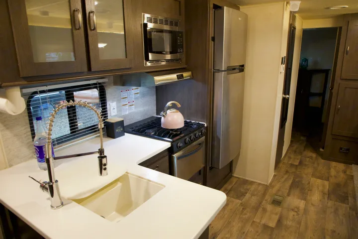 RV rental's modern kitchen: white countertops, sleek sink, microwave, stove/oven, refrigerator, and wood-look floors.. Forest River Salem 2018