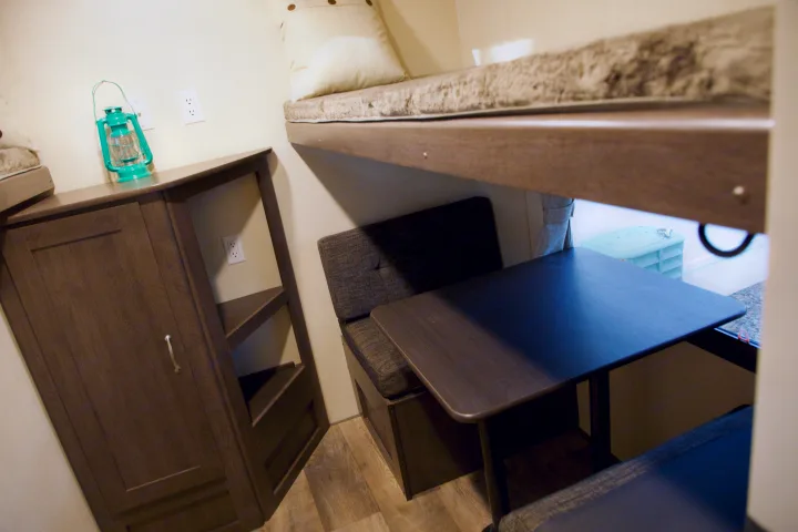 Cozy RV rental interior: upper bunk, dinette with table & benches, wood storage, and teal lantern.. Forest River Salem 2018
