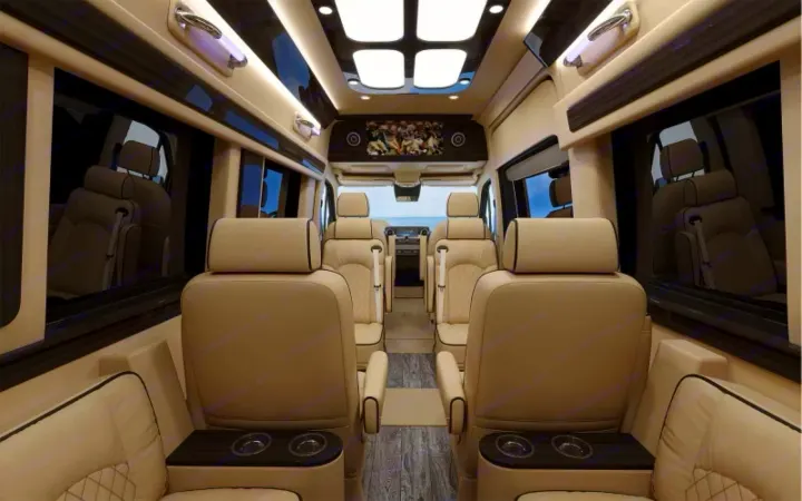 Luxurious custom van interior for RV rental, featuring spacious beige seating, overhead lighting, and a front-mounted TV. Ideal for comfortable group travel.. Ultimate Toys Coach- Midwest Automotive Daycruiser D6 2022