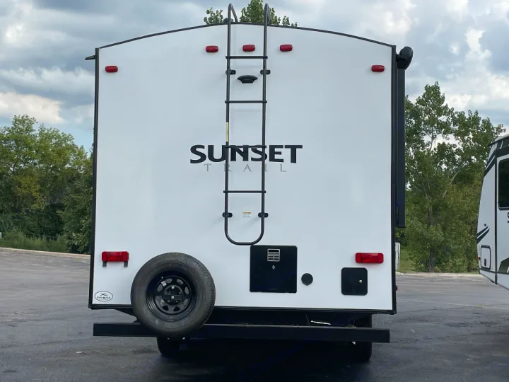 Rear view of a white Sunset Trail travel trailer RV, with a ladder and spare tire, ready for your next rv rental adventure.. Crossroads Sunset trail 242HB 2022