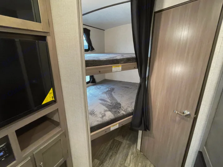 Cozy RV rental interior featuring twin bunk beds, a TV entertainment center, and a privacy door. Ideal for family adventures.. Crossroads Sunset trail 242HB 2022
