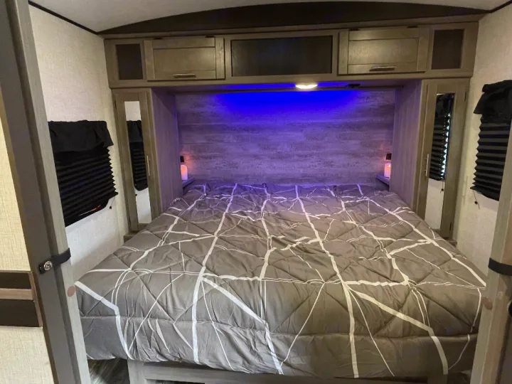 Experience comfort in this RV rental bedroom: a cozy bed, mirrored wardrobes, and ambient blue lighting for relaxing travel.. Crossroads Sunset trail 242HB 2022