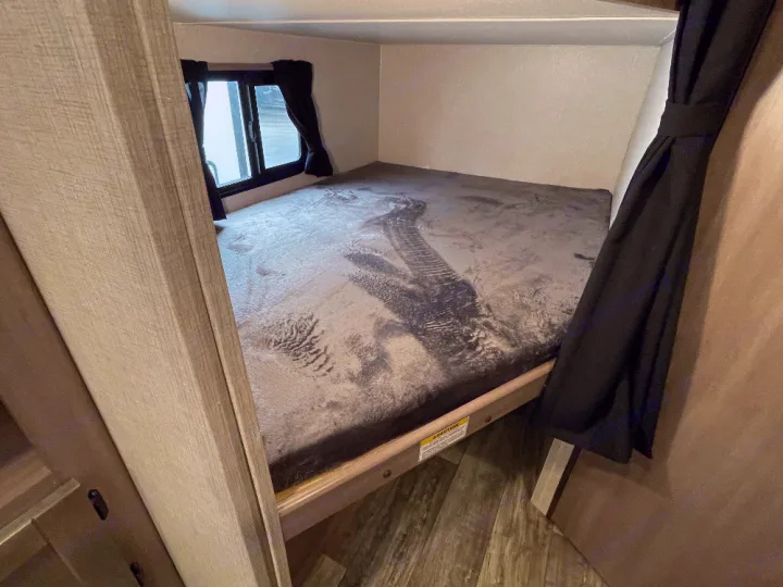 Cozy RV rental bunk bed, featuring a comfortable sleeping area with a window, black curtains, and wood-look interior.. Crossroads Sunset trail 242HB 2022