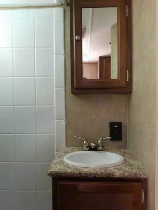 Compact RV rental bathroom featuring a sink, mirrored medicine cabinet, shower area, and a wall-mounted panel.. Coachmen Viking 2018