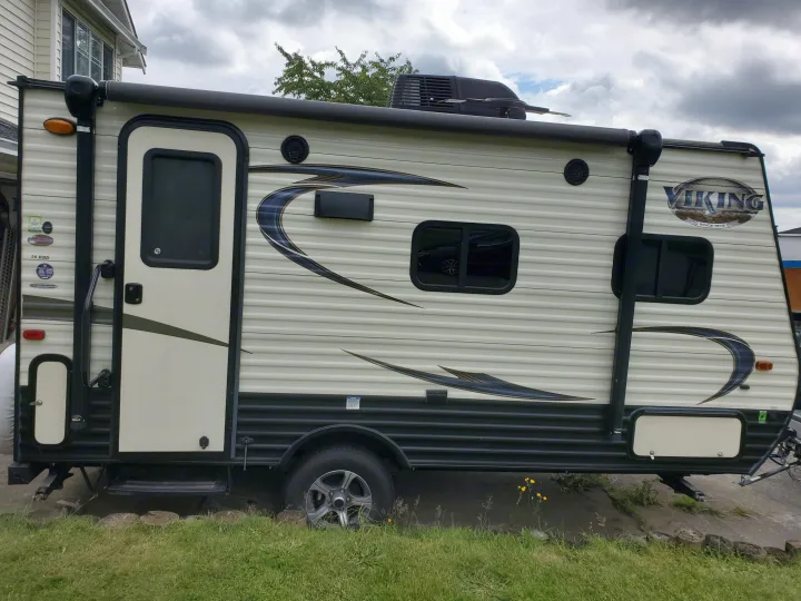 Viking travel trailer for RV rental, cream and dark, with an awning, windows, door, and roof-mounted AC unit.. Coachmen Viking 2018