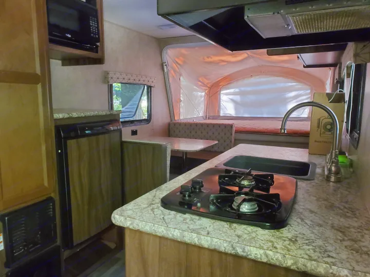Compact RV rental interior: kitchen with stove/sink, dinette, and well-lit pop-out bed area.. Coachmen Viking 2018