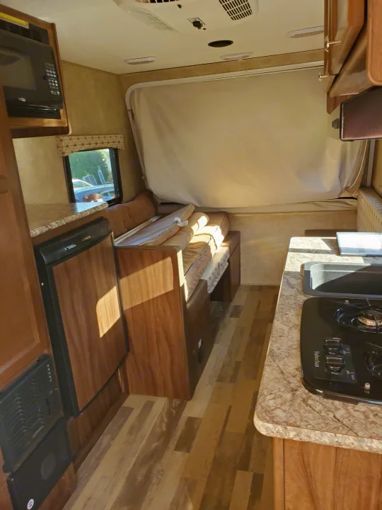 Inside a modern RV rental: microwave, fridge, and stove complement a convertible seating/bed area with wood-look flooring.. Coachmen Viking 2018