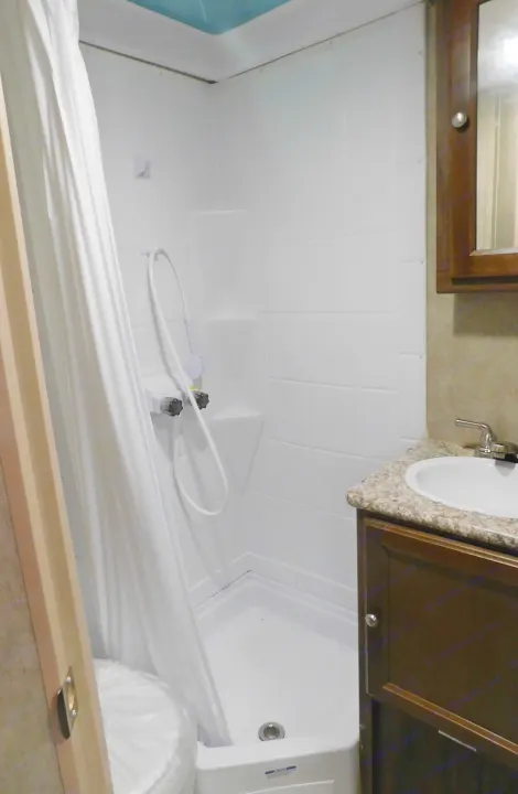 Compact RV rental bathroom featuring a shower stall with curtain, sink vanity, and toilet (wrapped).. Coachmen Viking 2018