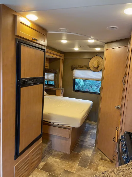 This RV rental features a compact, functional interior with a bed, fridge, and window overlooking trees.. Thor Freedom Elite 2017
