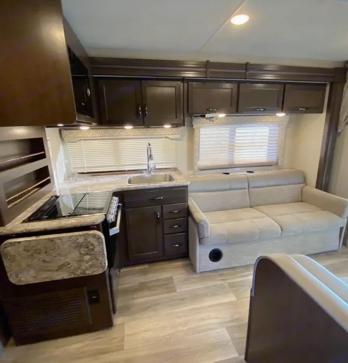Explore this RV rental's well-appointed interior: compact kitchen with stove & sink, cabinets, and comfy sofa.. Thor Motor Coach Freedom Elite 2019