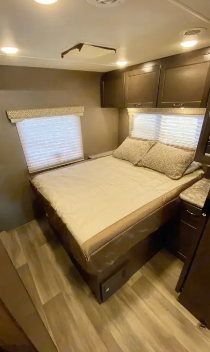 RV rental bedroom: a cozy bed, overhead cabinets, and windows with privacy blinds for comfortable travel.. Thor Motor Coach Freedom Elite 2019
