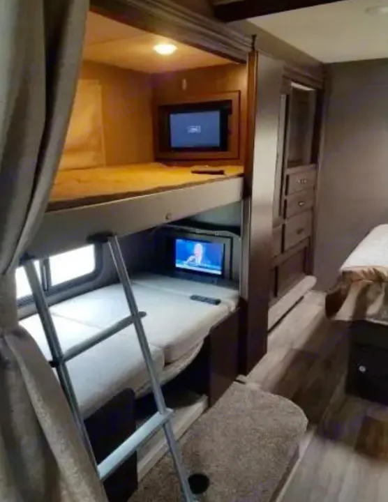 Compact RV rental bedroom with two bunk beds, each featuring a TV, a ladder, and built-in storage solutions.. Thor Motor Coach Freedom Elite 2019