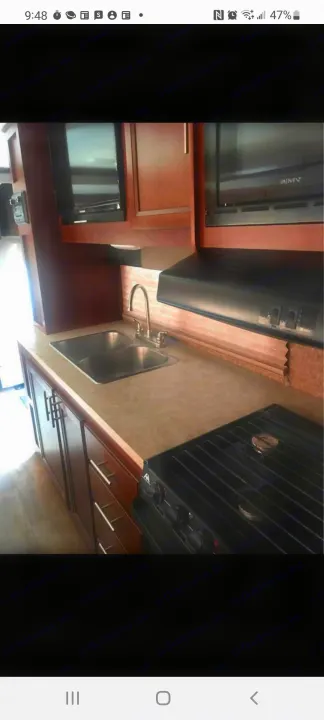 Spacious RV rental kitchen featuring a double sink, gas range, microwave, and rich wood cabinets.. Forest River Fr3 2015