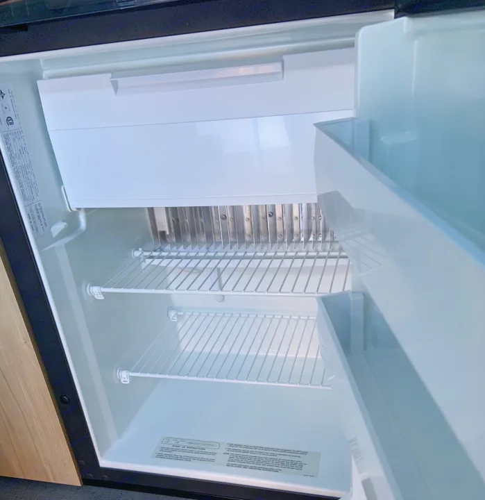 Clean interior of an RV rental refrigerator, showing wire shelves, a compact freezer, and operating instructions.. Safari Condo Alto R1723 Bunkhouse 2022