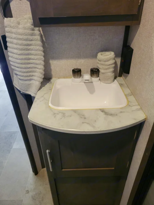 RV rental bathroom: compact sink area with a white basin, dark vanity, and textured hand towel.. Coleman 263 BH Lantern Edition 2021