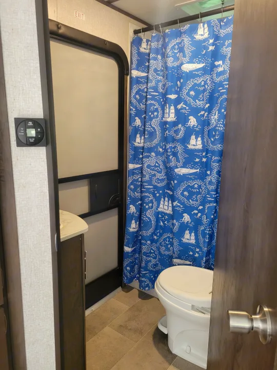 An RV rental bathroom featuring a blue nautical-themed shower curtain, toilet, and a compact control panel.. Coleman 263 BH Lantern Edition 2021
