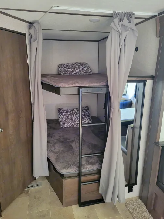 An RV rental's double bunk beds with plush bedding and privacy curtains for a comfortable, compact sleeping area.. Coleman 263 BH Lantern Edition 2021