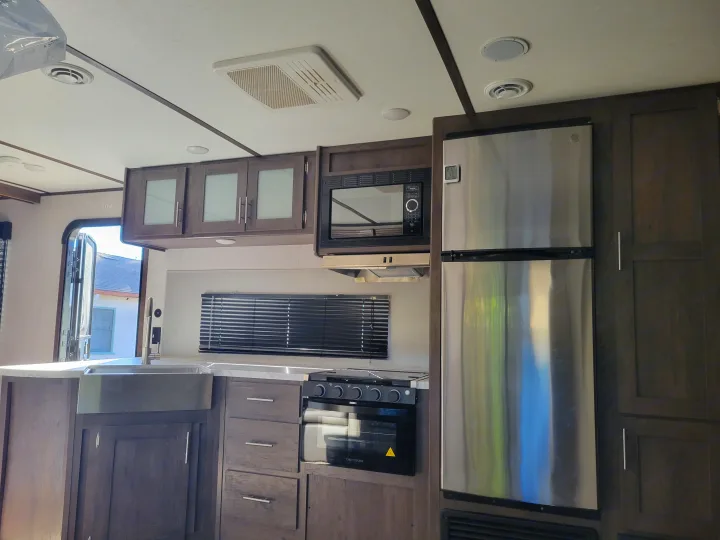 Inside a modern **rv rental**: a well-equipped kitchen with stainless steel appliances, dark wood cabinets, and a sink.. Coleman 263 BH Lantern Edition 2021