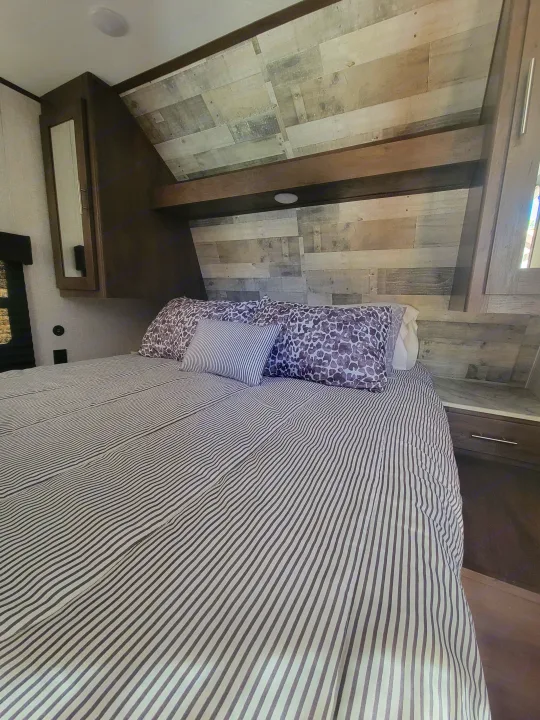 This RV rental bedroom features a bed with crisp striped bedding, accent pillows, and a stylish wood-look headboard.. Coleman 263 BH Lantern Edition 2021