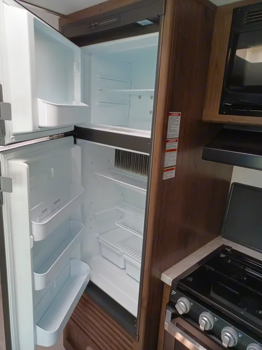 RV rental kitchen interior: open refrigerator, microwave, and range oven visible on wooden countertops. Compact design.. Keystone RV Passport Express 2019