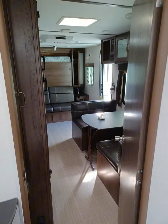 Inside an RV rental: a modern living space with dark dinette seating, light table, wood cabinetry, and a window.. Keystone RV Passport Express 2019