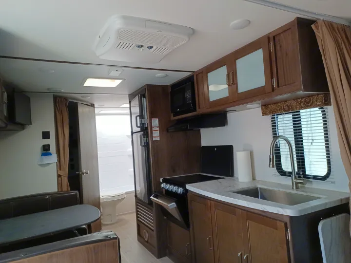 Modern RV rental interior with kitchen (sink, stove, microwave), dining area, and refrigerator. A bathroom entrance is visible.. Keystone RV Passport Express 2019