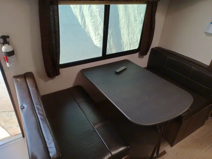This RV rental features a comfortable dinette with dark benches and a table, ideal for dining or work. A window is above the table.. Keystone RV Passport Express 2019