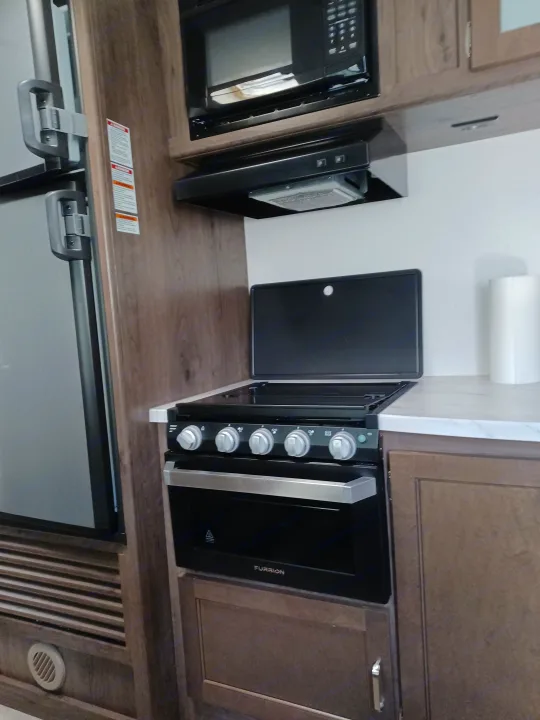 RV rental kitchen showcasing compact appliances: microwave, oven with controls, and refrigerator, all neatly integrated.. Keystone RV Passport Express 2019