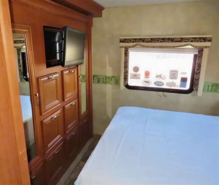 RV rental bedroom with a white-sheeted bed, window, mounted TV, and large wood wardrobe storage. Perfect for travel.. Forest River Other 2011