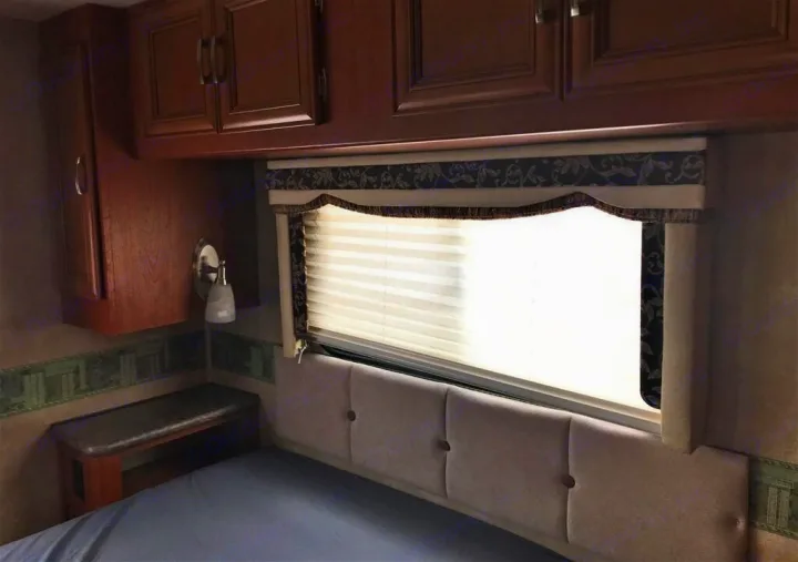Cozy RV rental bedroom featuring a comfortable bed, overhead cabinets, and a bright window with blinds.. Forest River Other 2011