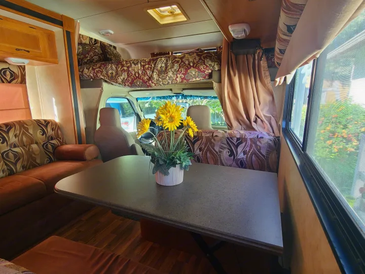 Step inside this cozy RV rental! Features a dining area with faux sunflowers, comfortable sofa, and overhead sleeping bunk.. Coachmen Freelander 2011