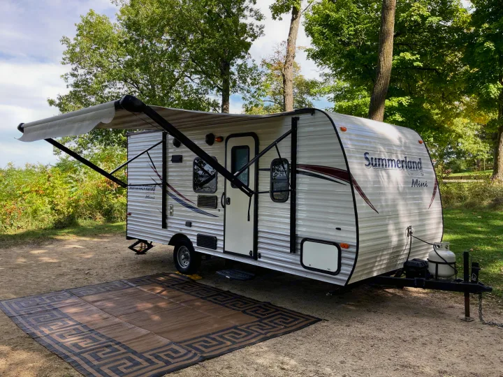 This Summerland Mini RV rental parked at a sunny campsite, featuring an extended awning and outdoor mat.. Keystone RV Summerland Mini 2016