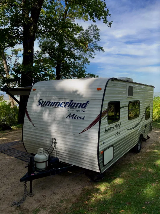 A white Summerland Mini RV rental is set up at a campsite, with trees and sky in the background, ready for outdoor adventure.. Keystone RV Summerland Mini 2016