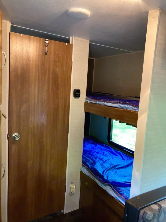 RV rental living space featuring a bunk bed, window view, and interior door with light and control panels.. Keystone RV Summerland Mini 2016