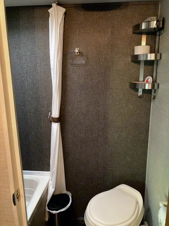 RV rental bathroom: A compact space with a white shower curtain over a small tub, a toilet, and corner shelves.. Keystone RV Summerland Mini 2016