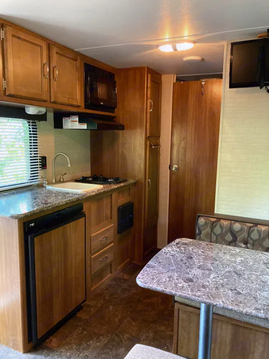 Spacious rv rental interior featuring a well-equipped kitchen with sink, stove, microwave, and a cozy dinette area.. Keystone RV Summerland Mini 2016